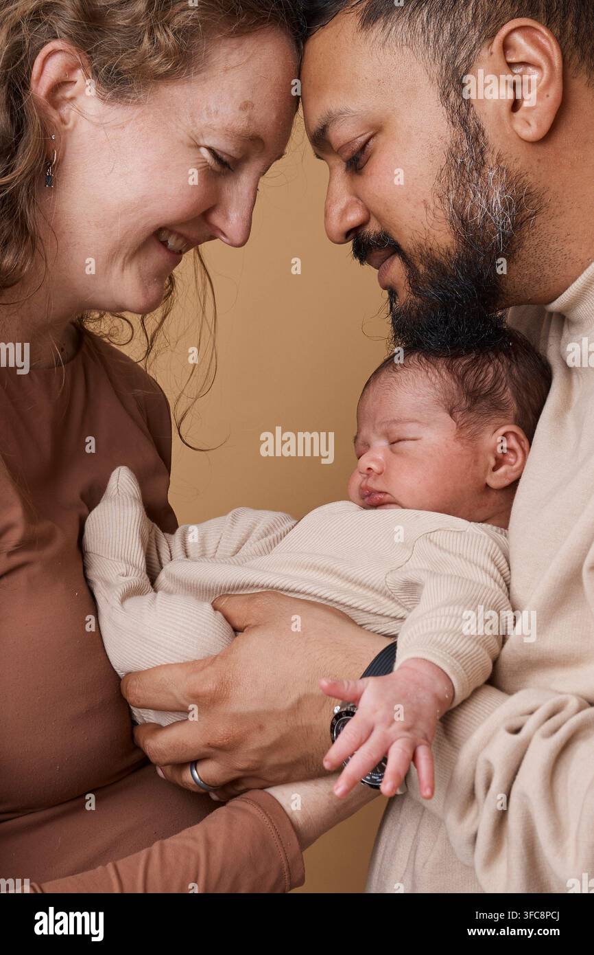 Zärtliches multikulturelles Familienporträt mit Neugeborenem, das von liebenden Eltern gehalten wird Stockfoto
