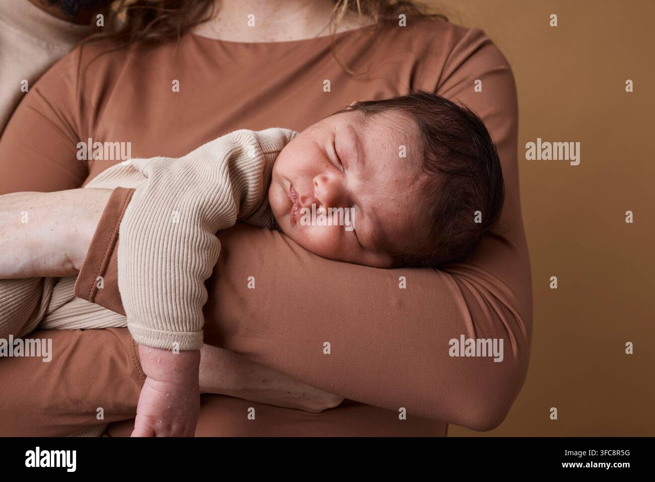Multikulturelle Mutter hält ein schlafendes Neugeborenes in einem warmen, neutralen Studio-Porträt und zeigt eine zärtliche Bindung Stockfoto