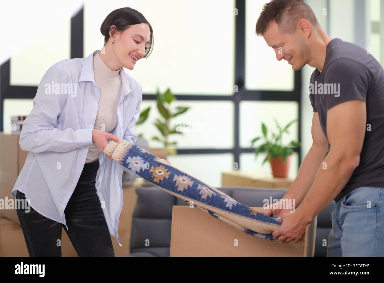 Glückliches Ehepaar nimmt Teppich aus der Box in der neuen Wohnung heraus Stockfoto