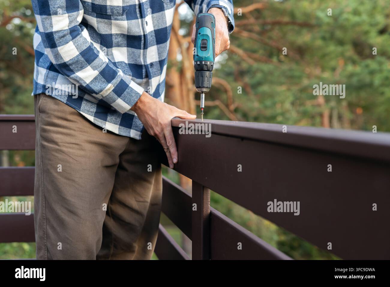 Arbeiter montiert Holzgeländer mit Schraubendreher während des Hausbaus Stockfoto
