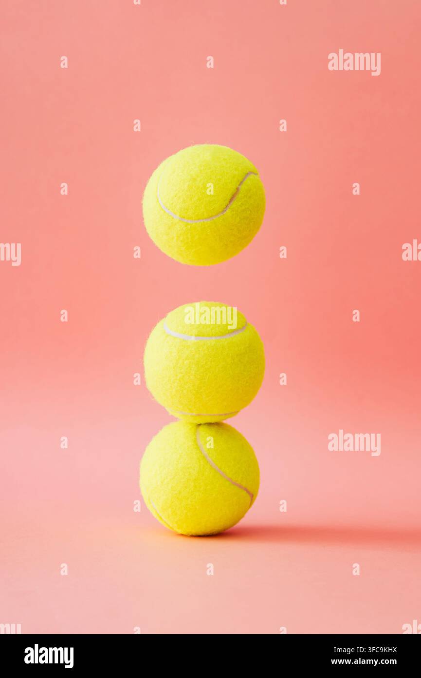 Drei Tennisbälle, die auf pastellrosa Hintergrund balanciert sind. Minimales Sportkonzept. Kreative Tennisballidee. Tennisästhetik. Stockfoto