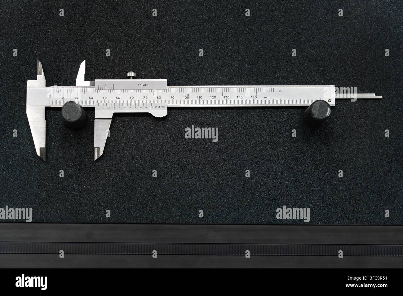 Präzisions-Edelstahl-Vernier-Zang mit metrischen und imperialen Messskalen auf einer schwarzen Oberfläche für genaue Dimensionsmessung Stockfoto