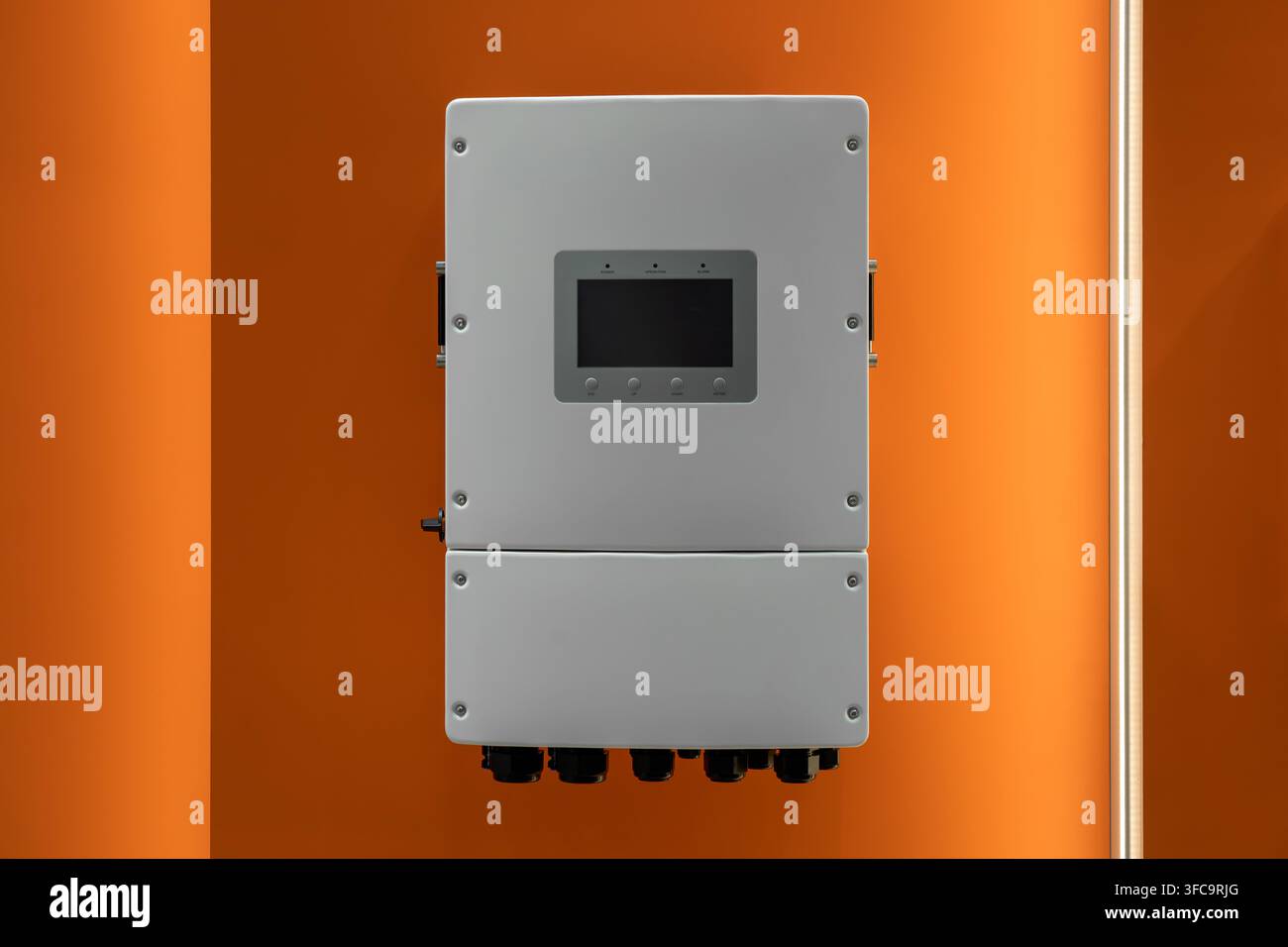 Weiße Hybrid-Solarwechselrichtereinheit mit Kühlventilatoren und DC-Schalter, installiert an einer beleuchteten orangefarbenen Wand Stockfoto