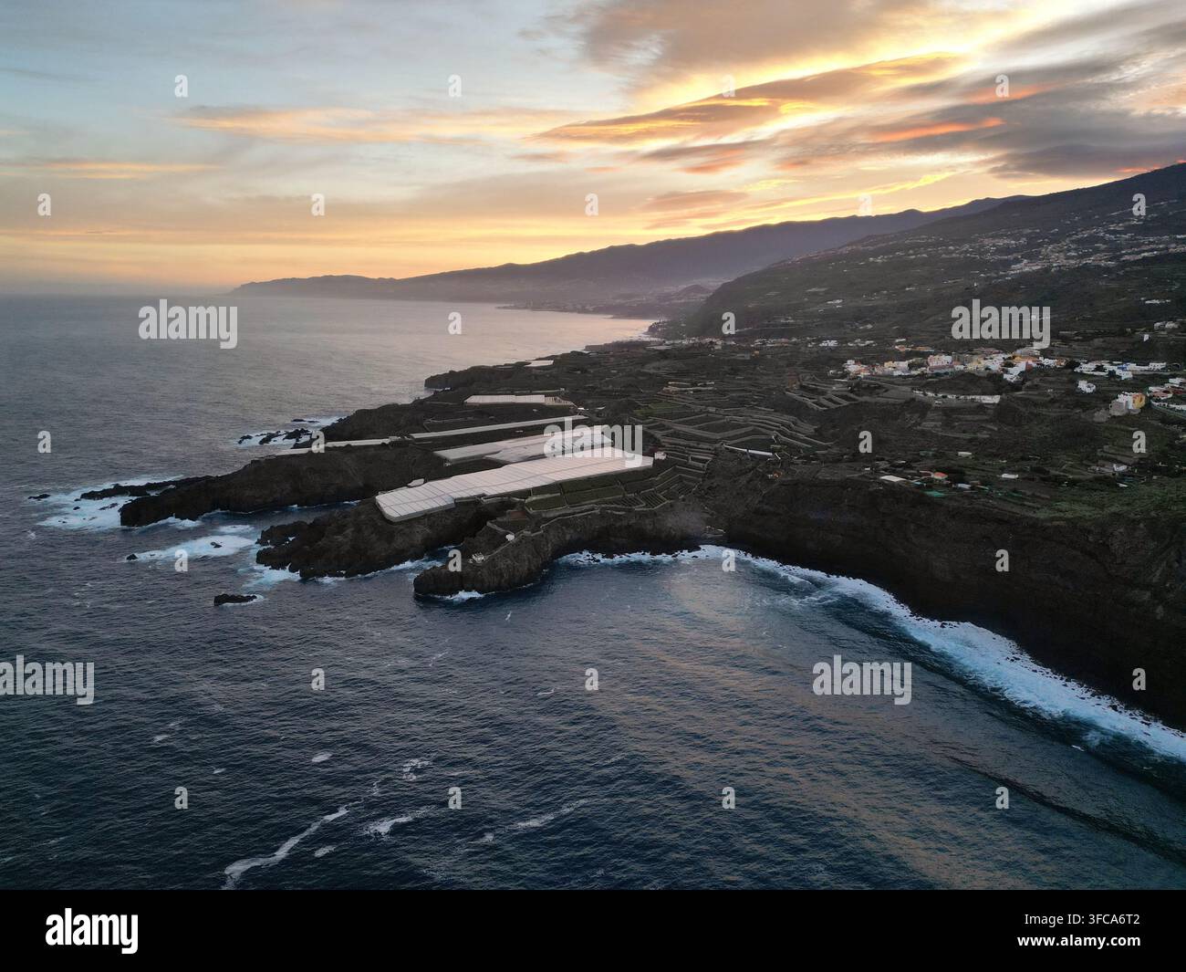 Luftbild der zerklüfteten Küste bei Sonnenuntergang, mit vulkanischen Klippen, landwirtschaftlichen Gewächshäusern und dem Atlantischen Ozean in Icod de los Vinos, Teneriffa Stockfoto