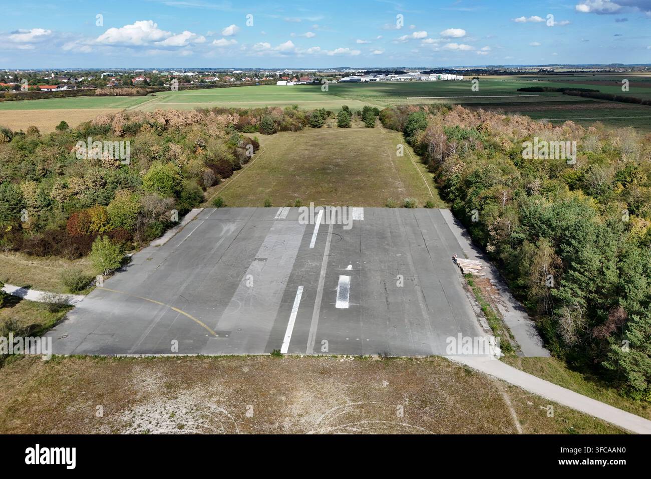 Verlorener Ort in München. Die verlassene Startbahn des ehemaligen Flughafens München-Riem inmitten einer herbstlichen Landschaft. Das Luftbild zeigt ein verbliebenes Stück der alten asphaltierten Start- und Landebahn des ehemaligen Flughafens München-Riem. Die graue Asphaltfläche h Stockfoto