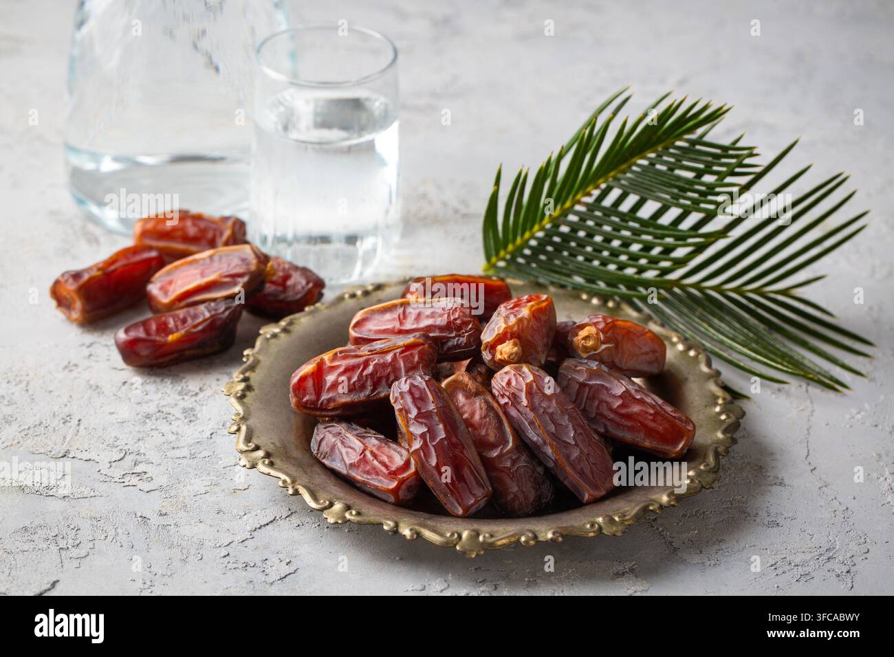 Glas Wasser und trockene Datteln auf einem traditionellen Teller über Marmorhintergrund für das Ramadan-Iftar-Konzept Stockfoto