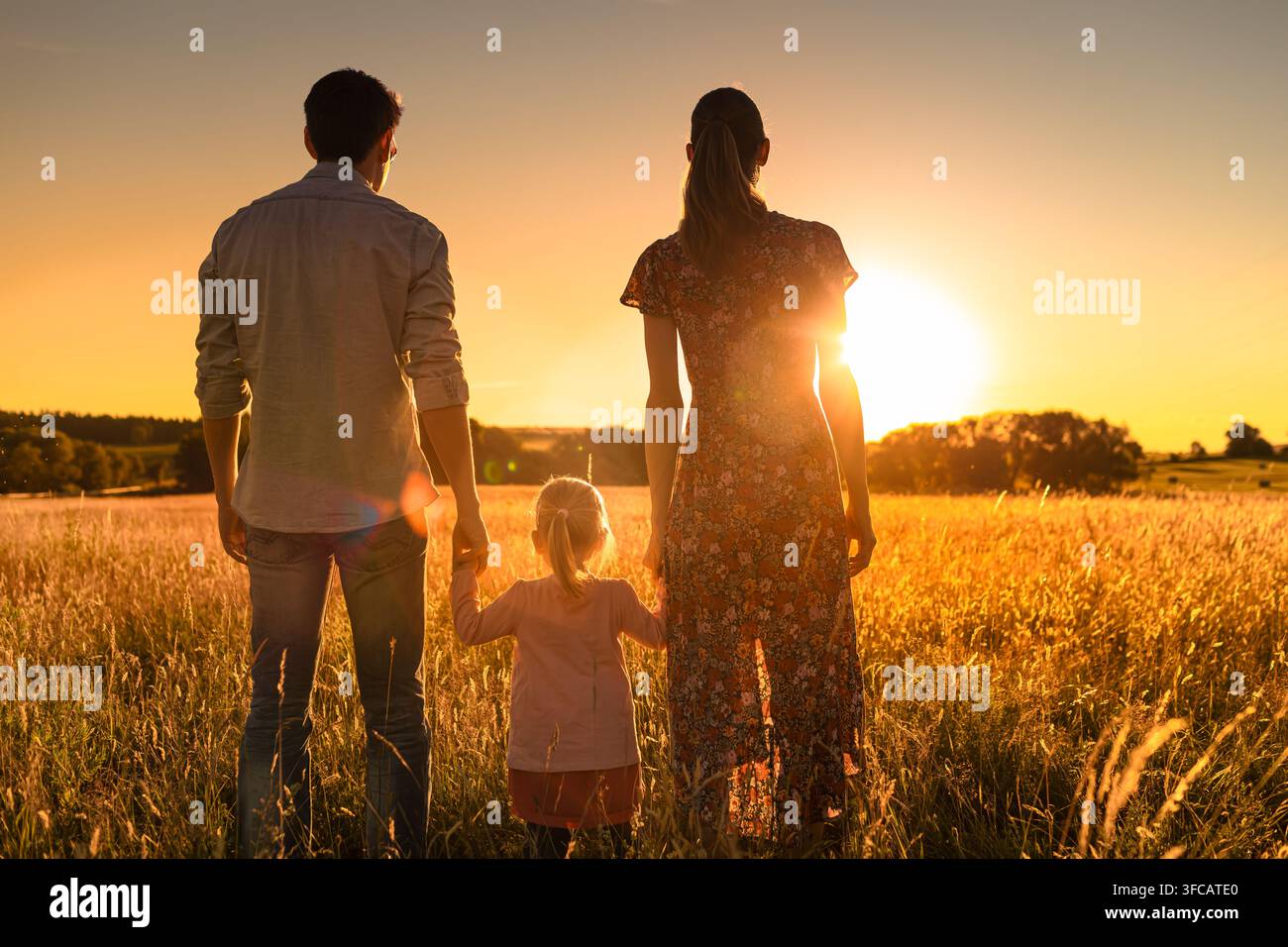 Mutter und ihre beiden Kinder sitzen zusammen auf einem Feld und blicken zum Sonnenuntergang hinaus. Mutterschaft und glückliche Familie in der Natur als Konzept. Stockfoto