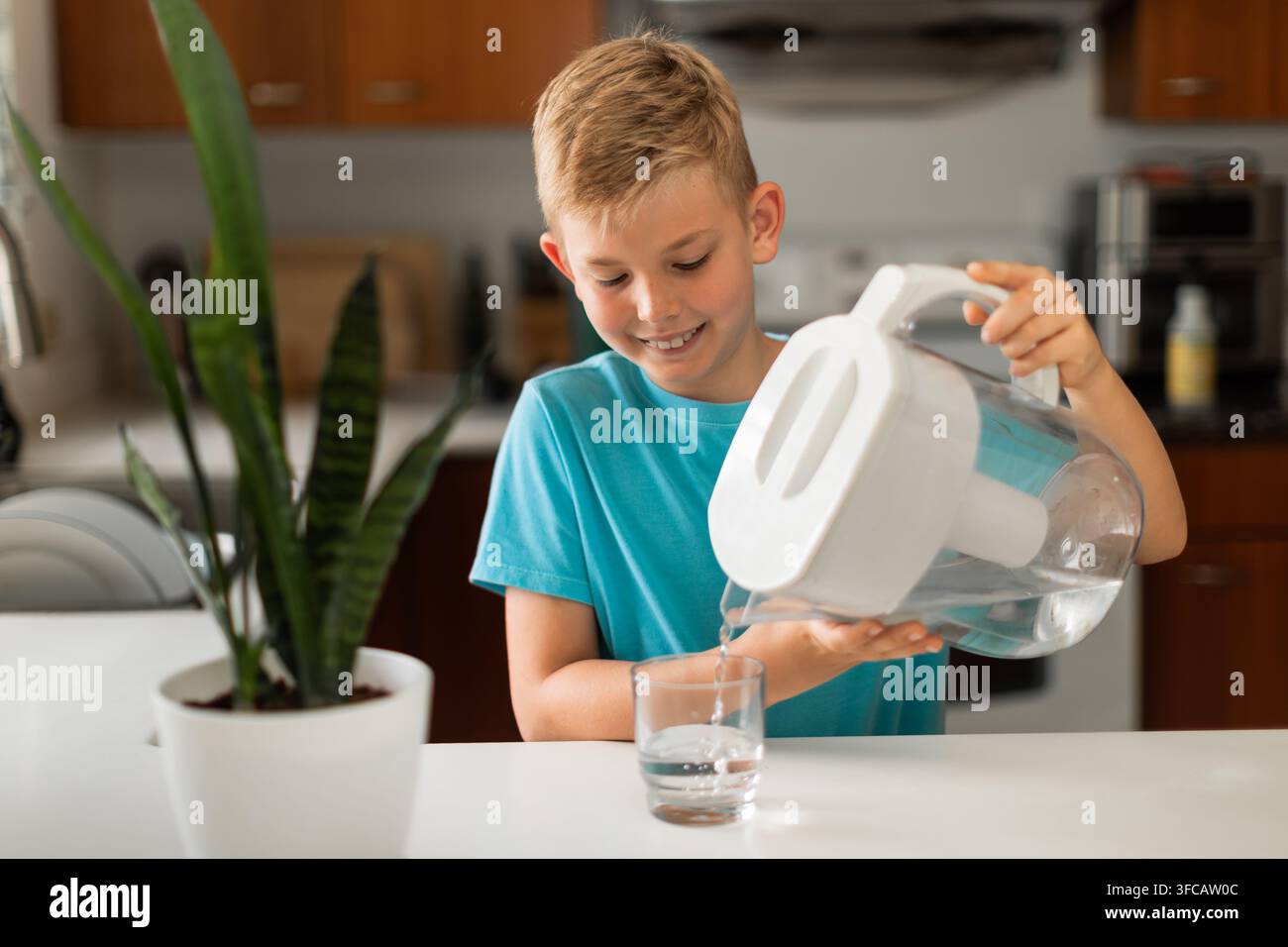 Junge, der Trinkwasser aus einem Filterkanister gießt. Gesunder Lebensstil zu Hause. Stockfoto