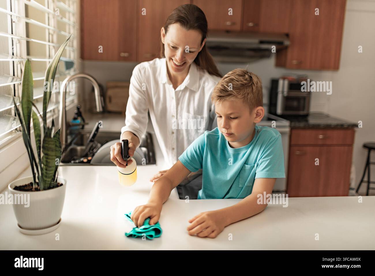 Mutter bringt Sohn das Reinigen der Küchentheke mit Spray und Tuch bei, Elternverantwortung, Hygiene, Familienlebensstil und Haushaltsaufgaben-Konzept Stockfoto