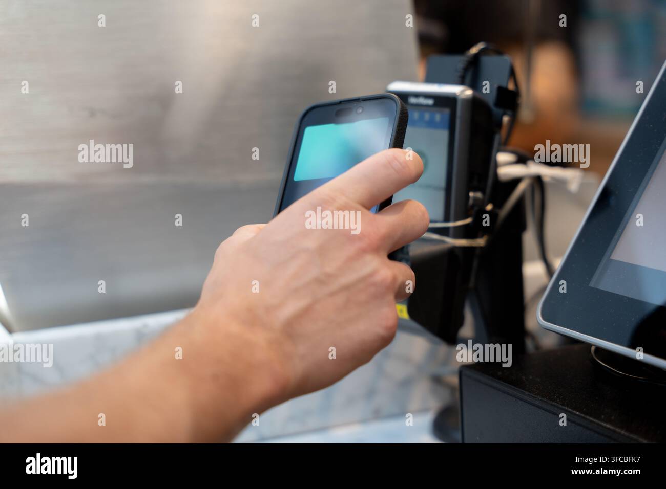 Zuschnittbild einer Männerhand, die ein Smartphone hält, um eine digitale Zahlung mit einer mobilen Geldbörse über kontaktloses Bezahlen an einem POS-Terminal vorzunehmen Stockfoto