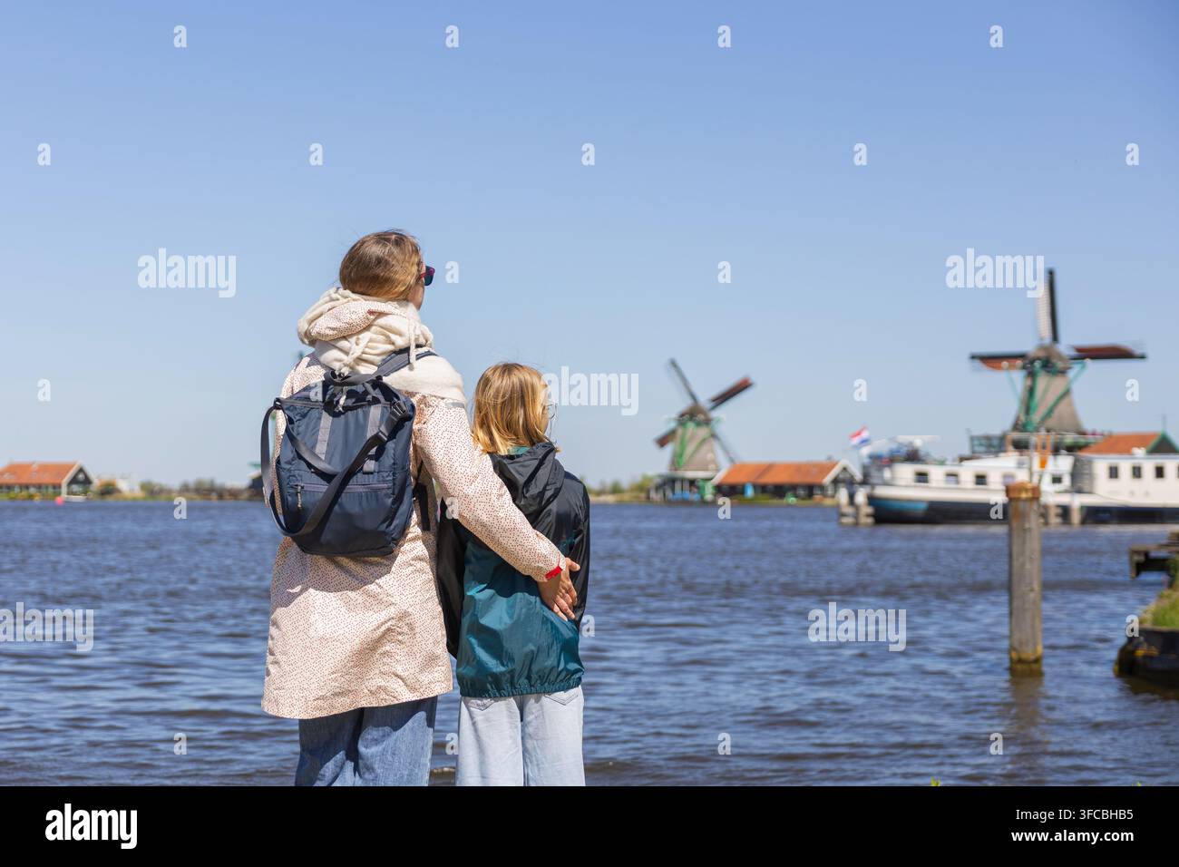 Mutter und Tochter stehen am Wasser und blicken auf Windmühlen in den Niederlanden während eines Familienausflugs. Es ist ein sonniger Tag mit klarem Himmel. Stockfoto