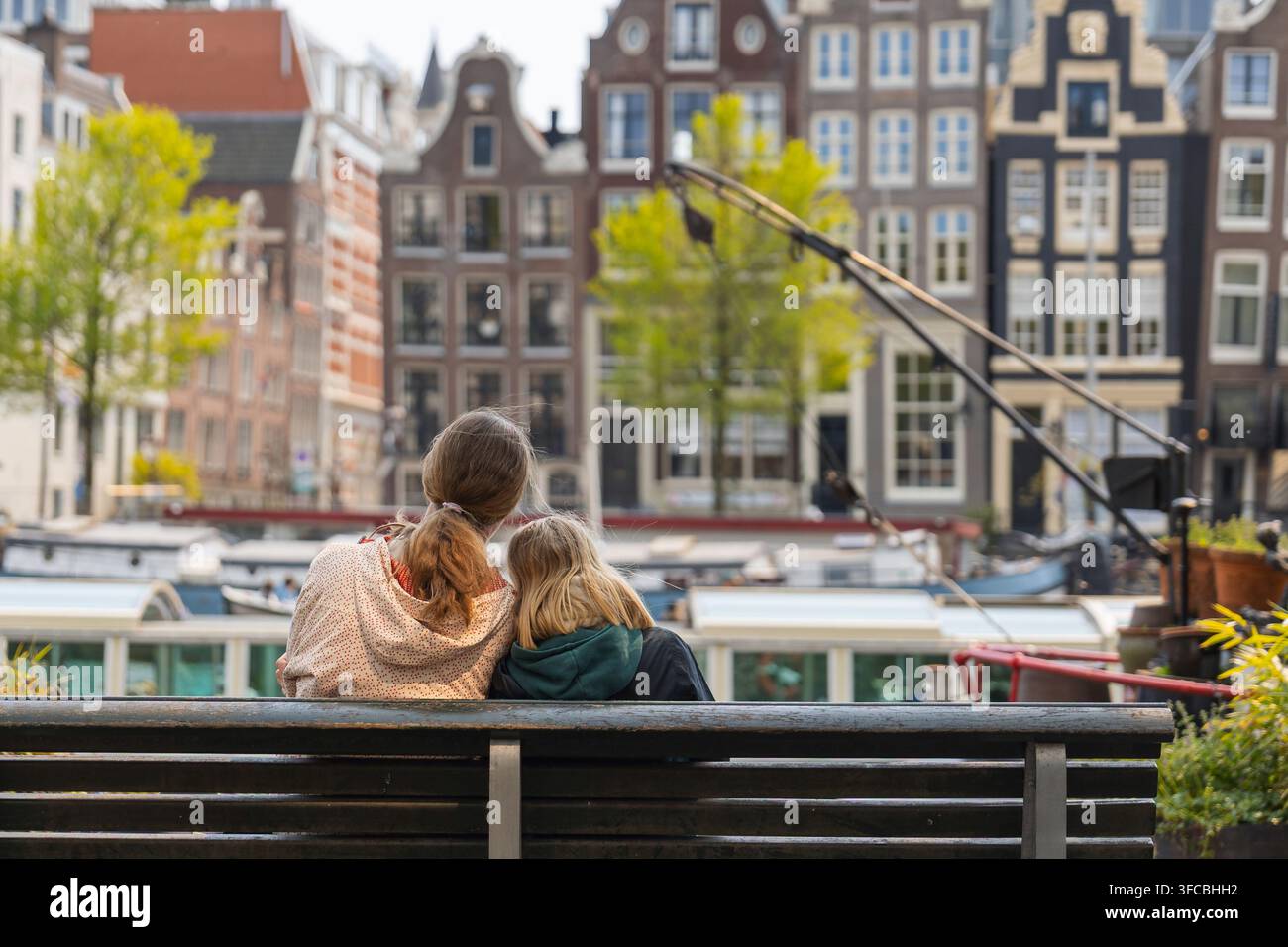 Eine Mutter und ihre Tochter sitzen zusammen auf einer Bank am Kanal in Amsterdam. Sie genießen ihre Zeit während eines Familienurlaubs in Europa. Stockfoto