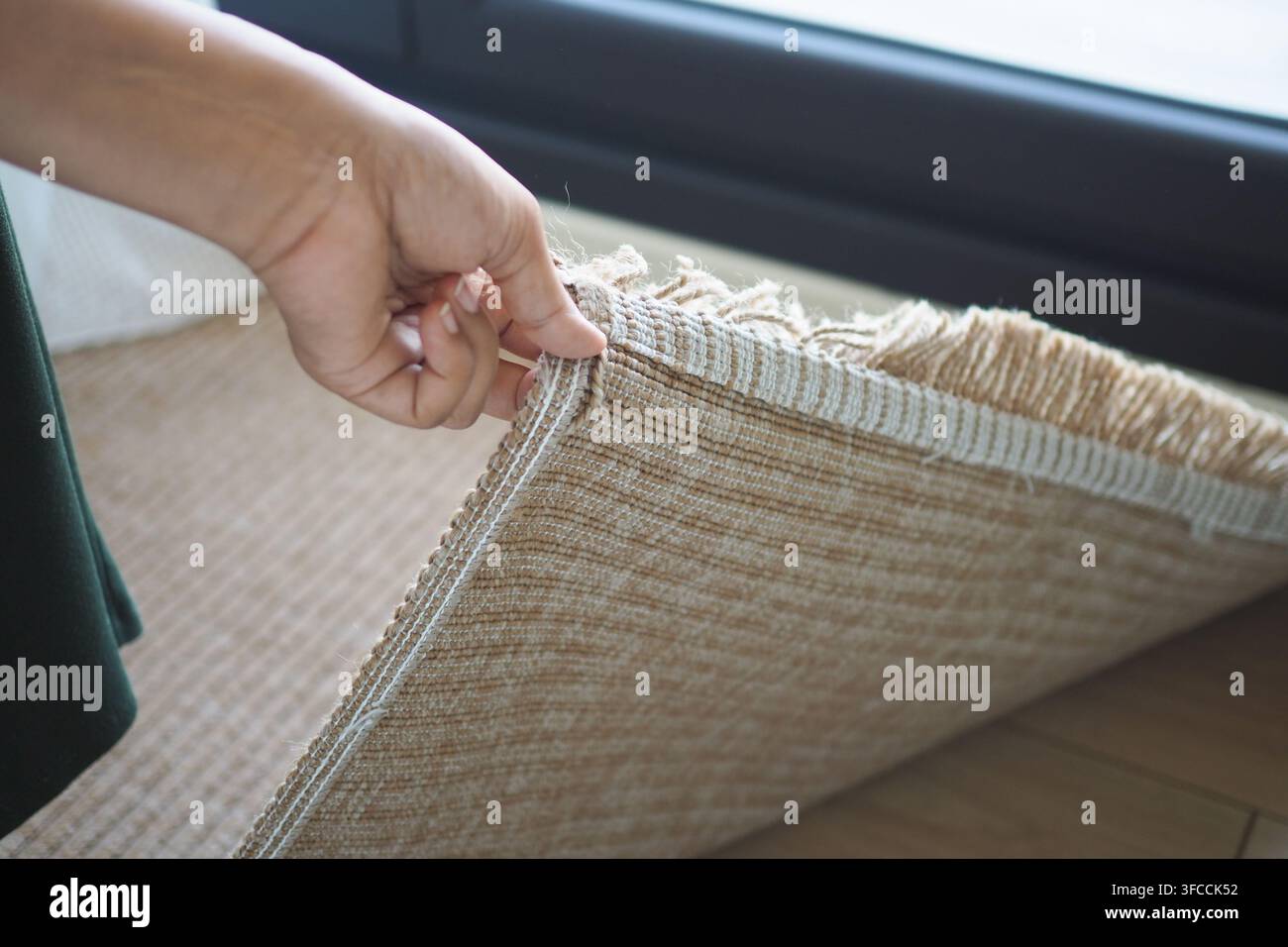 Hand, die einen Teppichrand in einem hellen Raum hält Stockfoto