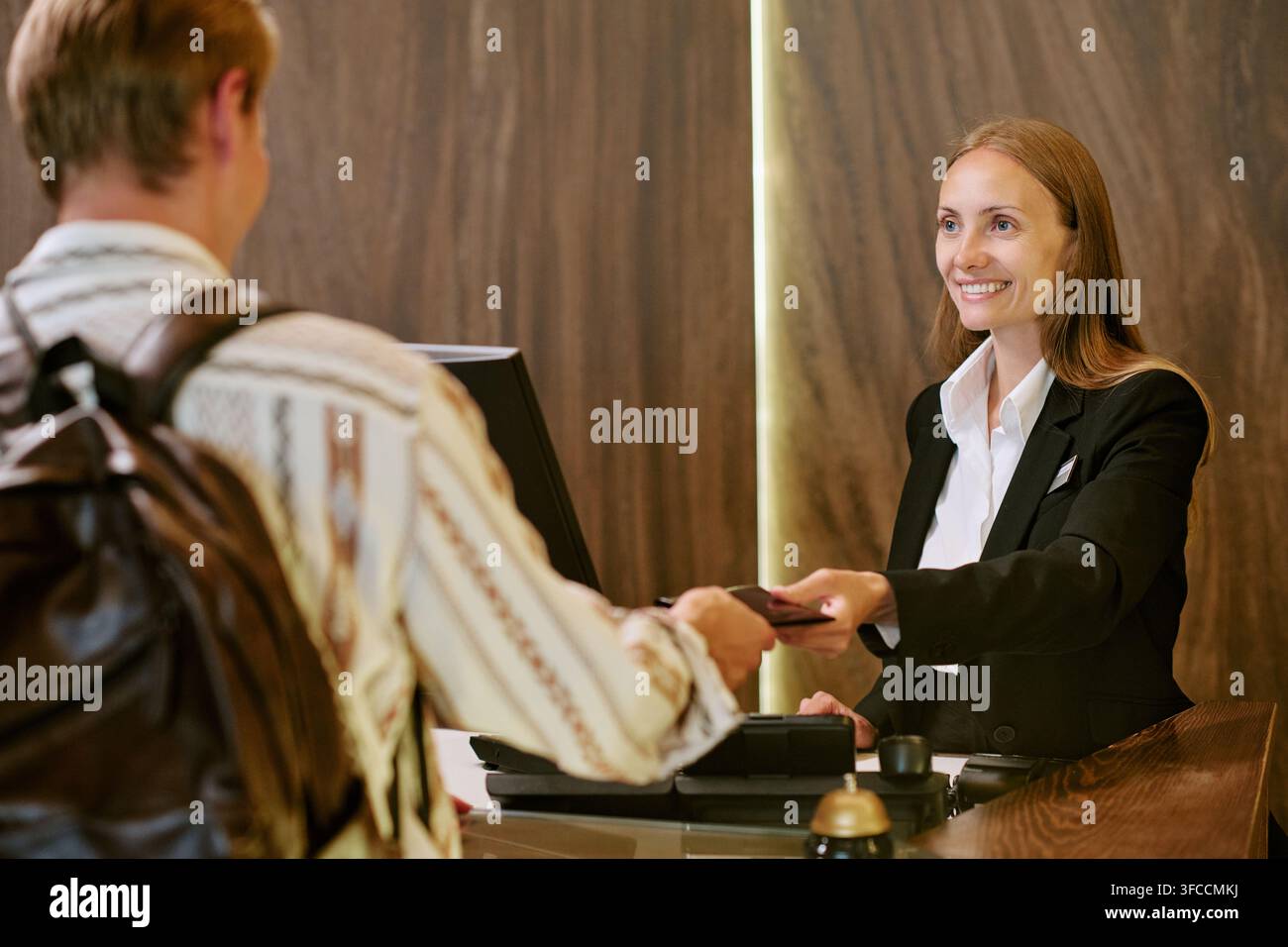 Lächelnde weibliche Rezeptionistin begrüßt Mann am Hotel-Check-in-Schalter Stockfoto