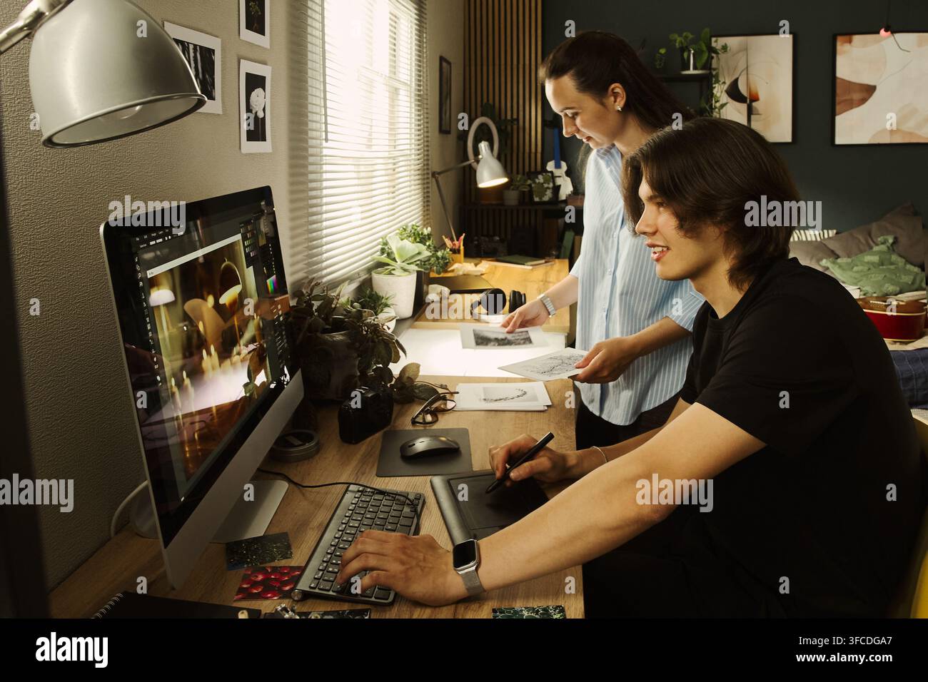Junges multikulturelles Designer-Paar arbeitet am Computer im Homeoffice, bearbeitet Fotos mit einem Grafiktablett. Perfekt für Remote-Arbeit und kreatives Agentiermarketing Stockfoto