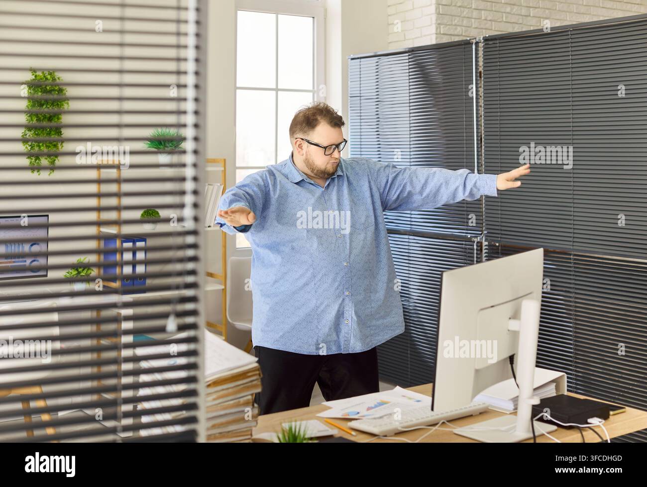 Fröhlicher Büroangestellter tanzt in der Nähe des Computers nach Erfolg mit Berichten und Akten Stockfoto