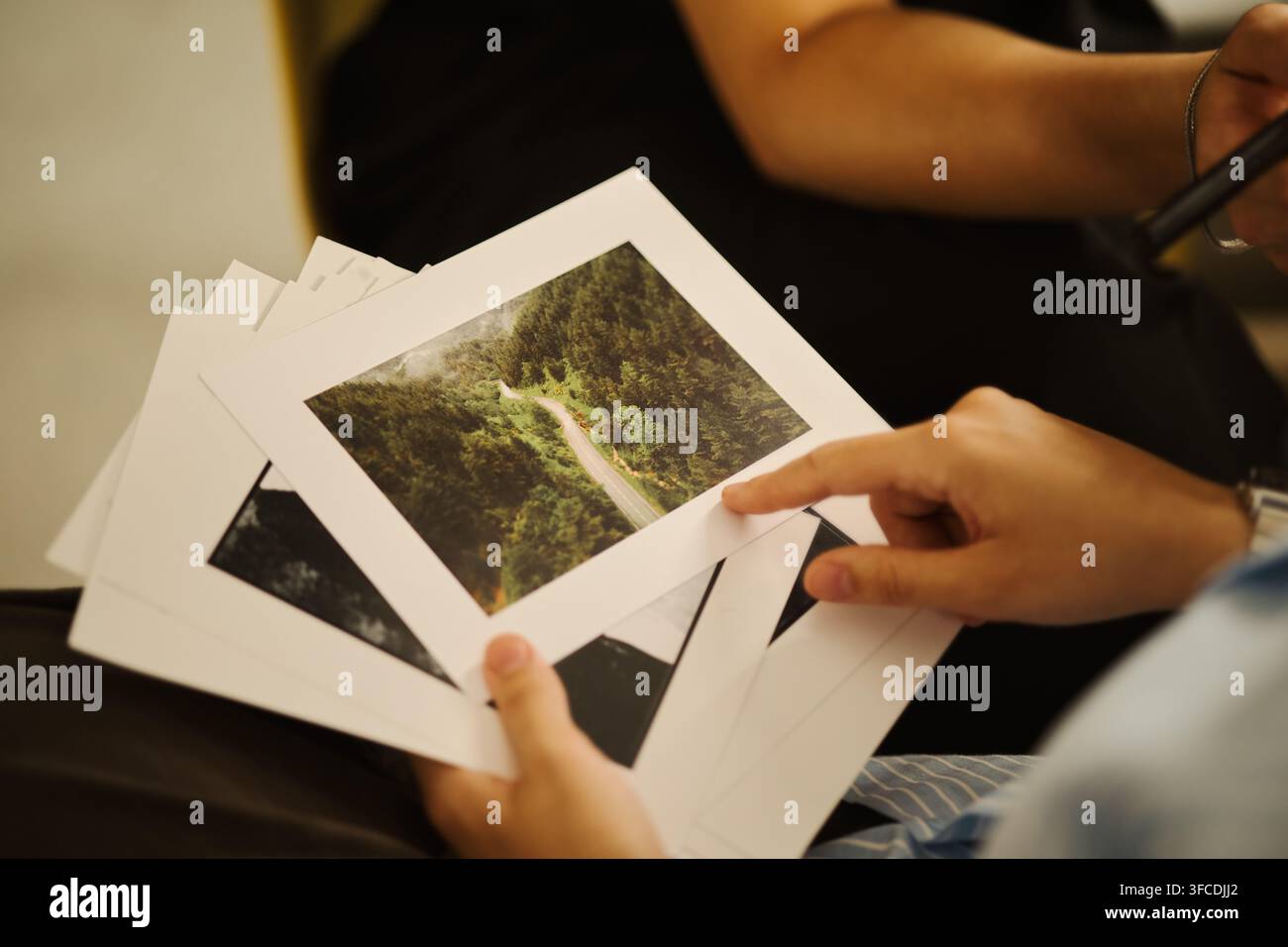 Hände eines jungen asiatischen Mannes, der gedruckte Landschaftsfotos während einer kreativen Portfoliobesprechung hält und darauf zeigt, repräsentierend Fotografiegeschäft und künstlerische Kuratierung, Nahaufnahme Stockfoto