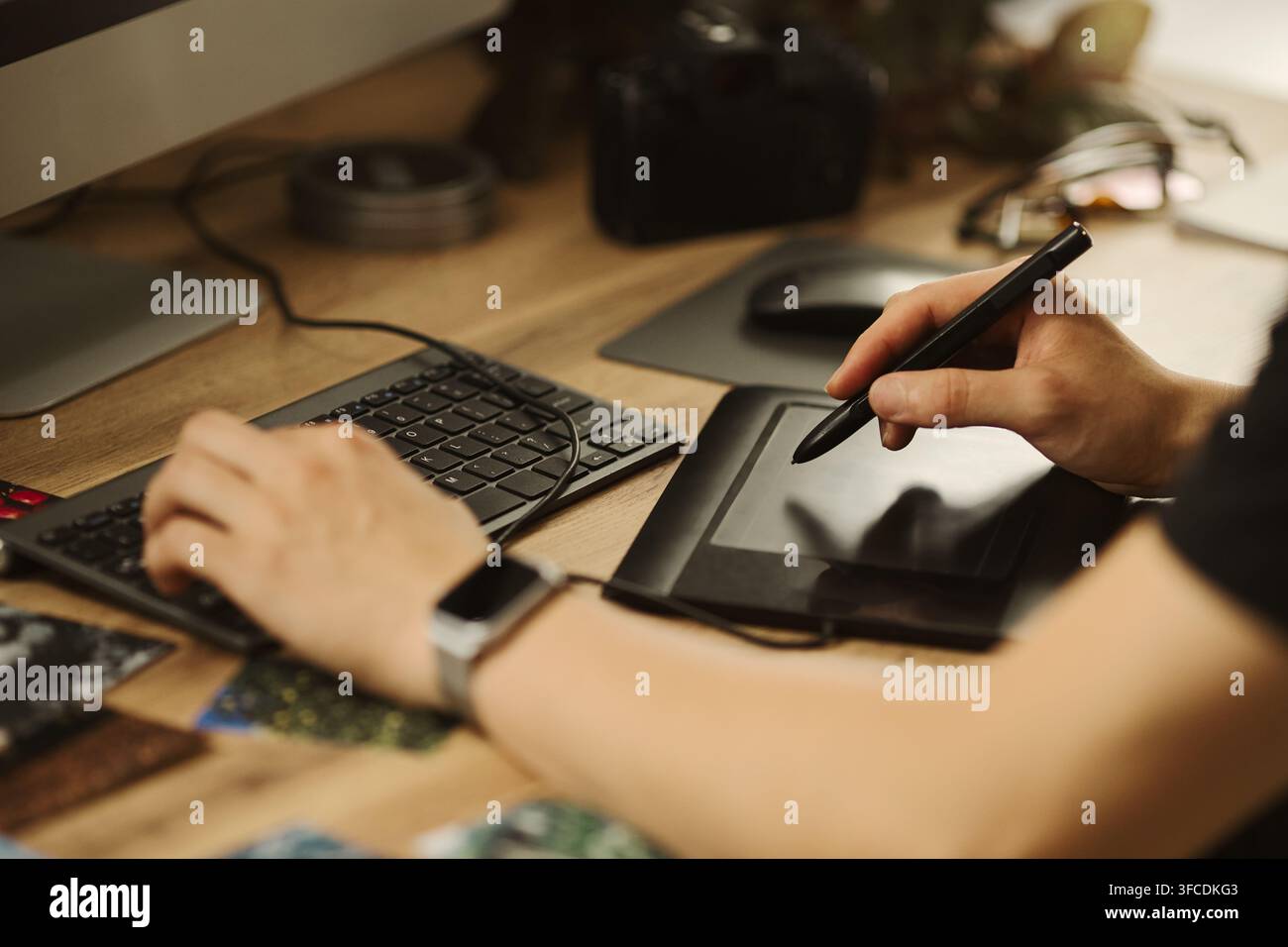 Hände eines männlichen Designers, die ein Grafiktablett und eine Tastatur an einem Holzschreibtisch verwenden. Bild repräsentiert die digitale Kunstschöpfung, geeignet für Marketing von Kreativagenturen Stockfoto
