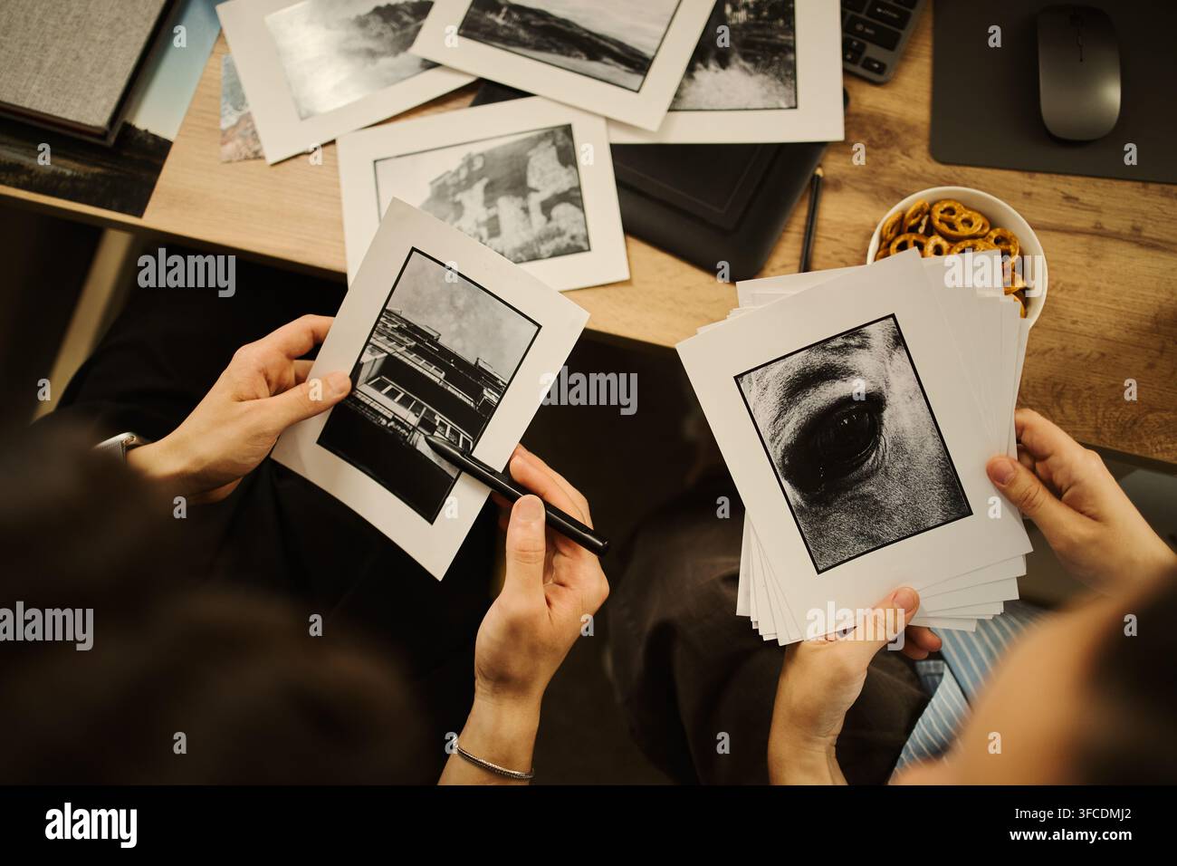 Hände nicht identifizierbarer Redakteure, die schwarze und gedruckte Fotos auf dem Schreibtisch halten, Portfolio durchsehen. Bild geeignet für die Promotion einer Kreativagentur oder einer Fotoschule Stockfoto