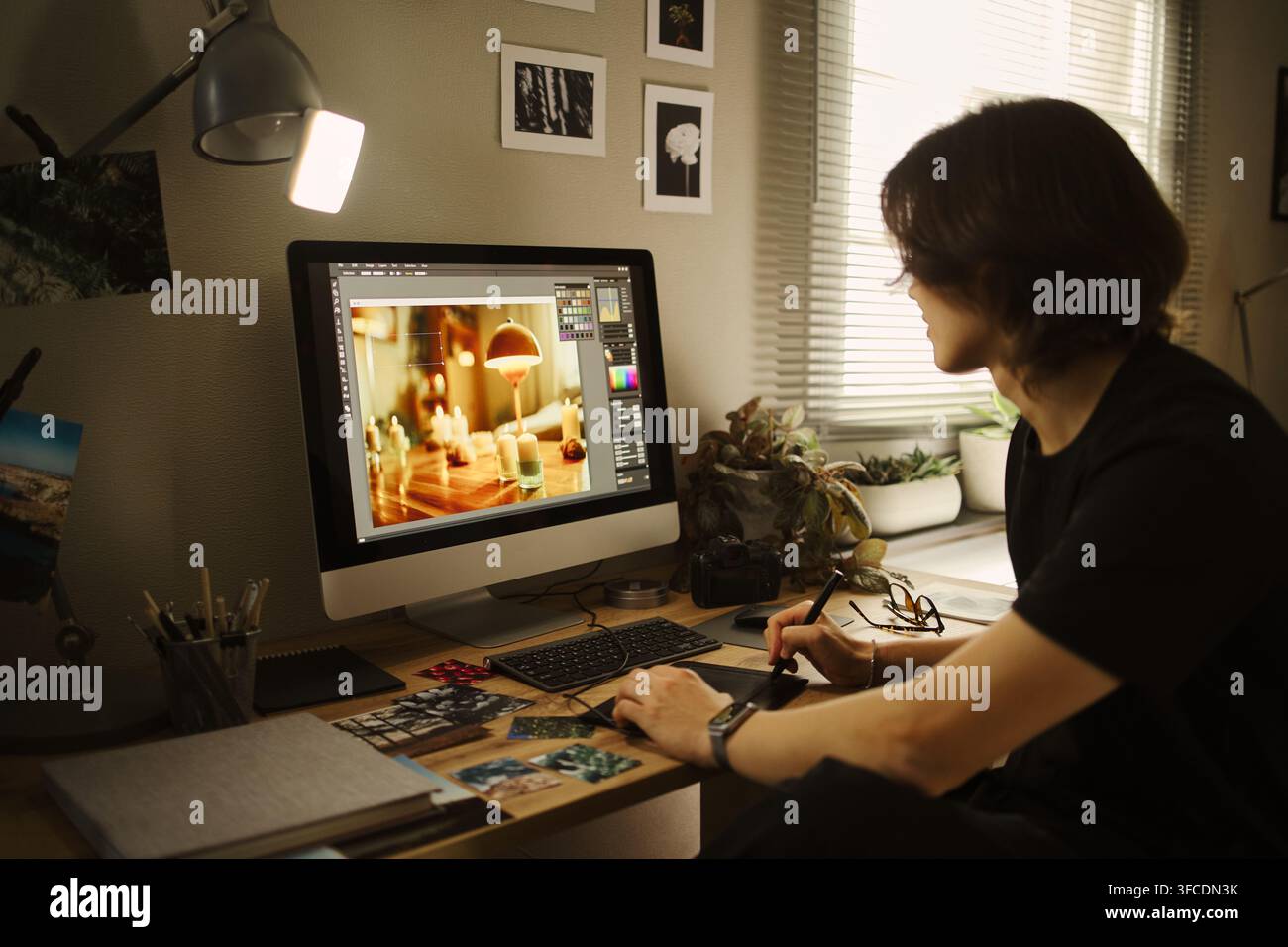 Junger asiatischer Mann bearbeitet ein Foto am Computer mit einem Grafiktablett im Home-Office. Das Bild repräsentiert Fernarbeit und kreativen Beruf, geeignet für die Vermarktung von Freelancern Stockfoto