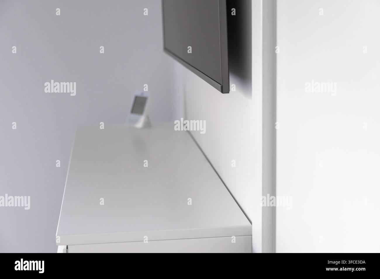 Ein schlanker, zeitgenössischer Wohnraum mit einem Flachbildfernseher, der über einer weißen Kommode montiert ist, auf der ein kleines elektronisches Gerät steht Stockfoto