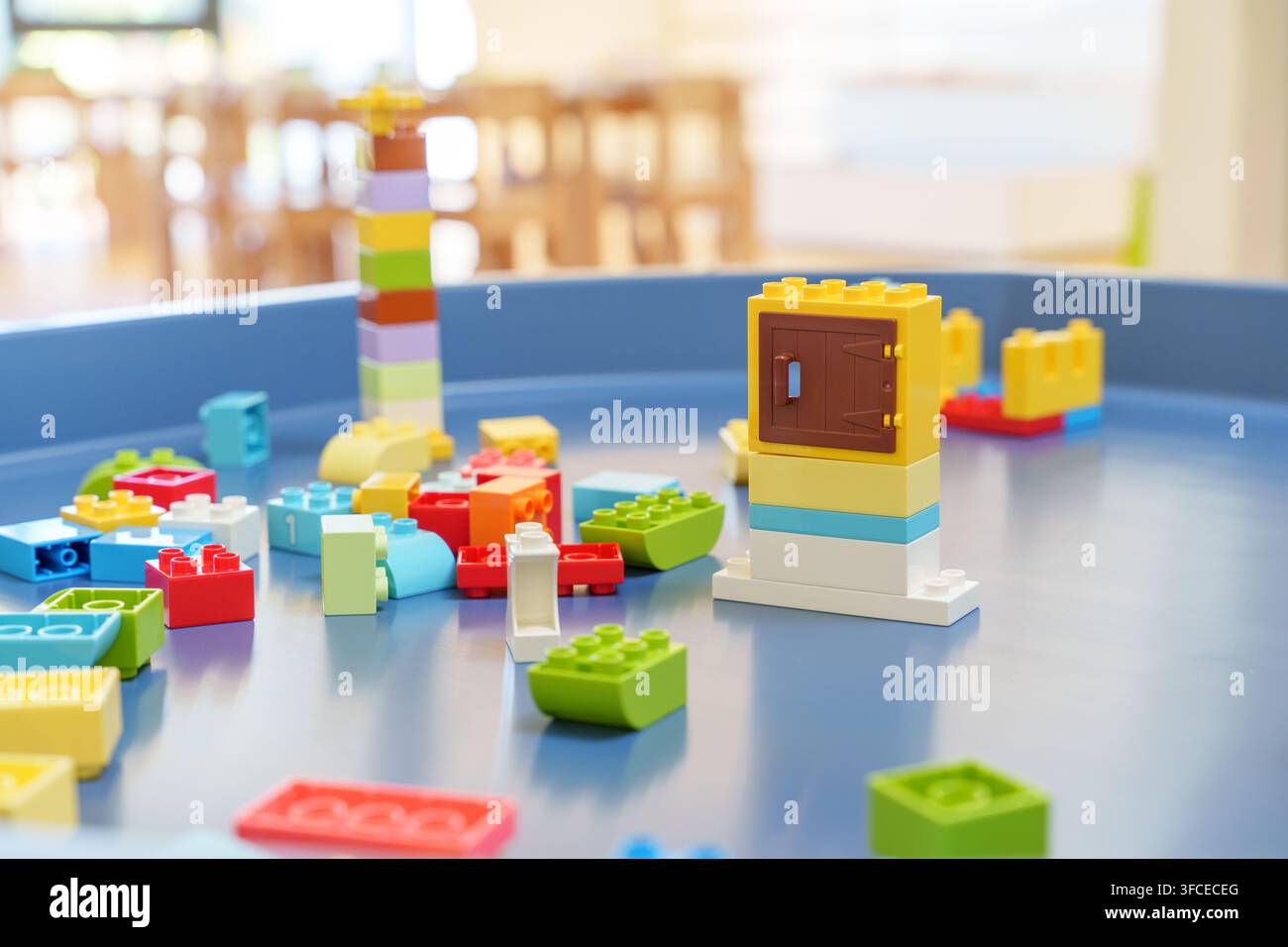 Bunte Plastikbausteine, die auf blauem Spieltisch in hellem Klassenzimmer verstreut sind, Konzept für frühe Kindheitserziehung und kreatives Spielen. Stockfoto