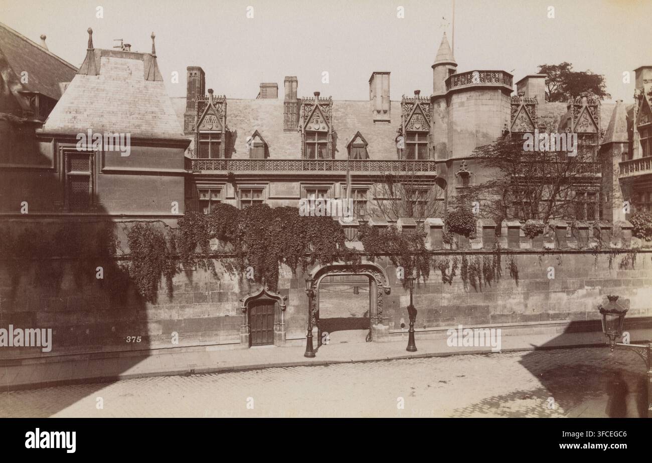 Musée de Cluny in Paris, Paris. – La Musée de Cluny, Fotografie, Nummer: „889“, Nummer: „375“, Inschrift: „Paris“, Fotograf: Höhe 119 mm x Breite 184 mm, Dauerausstellung, Museum, Hôtel, d.h. kleiner Palast in der Stadt, Paris, Musée de Cluny. Eine sepiafarbene Ansicht eines verzierten Steinbaus und einer Hofmauer mit dekorativen Fenstern und steil geneigten Dächern, die mit geschnitzten Gauben und Schornsteinen versehen sind. Ein zinnenbesetzter Wall verläuft entlang der oberen Mauer, mit herabfallendem Efeu und Kletterpflanzen, die über den Stein hängen. Ein großes gewölbtes Tor ist in die Mauer eingelassen und öffnet sich nach innen, flankiert von einer kleineren Tür mit Stockfoto
