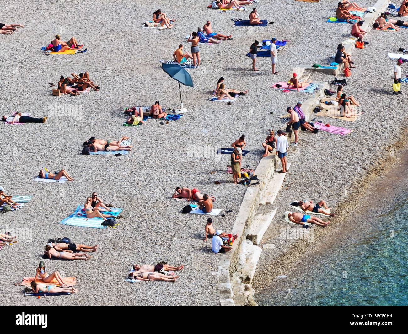 Ein lebhafter Kieselstrand in Dubrovnik im Sommer, an dem sich vielfältige Touristen an der Adriaküste sonnen und entspannen. Stockfoto