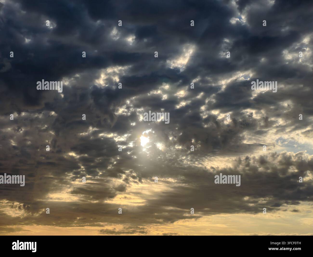 Ein dramatischer, stimmungsvoller Himmel, an dem goldenes Sonnenlicht durch dicke, dunkle Gewitterwolken bricht und eine kraftvolle Atmosphäre der Hoffnung und Widerstandsfähigkeit schafft. - Smartphone-aufgenommenes Stockfoto