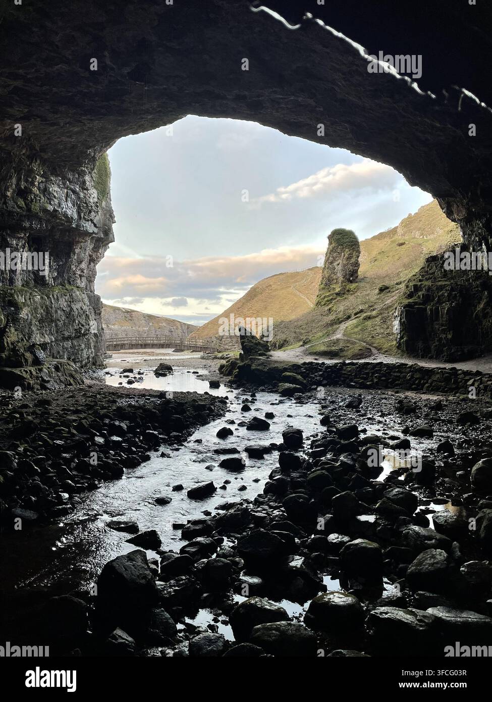 Dramatische Ansicht aus der Smoo-Höhle nahe Durness in den schottischen Highlands, mit Blick über den felsigen Höhlenboden und den Bach hin zur rauen Landschaft - Smartphone-aufgenommenes Stockfoto