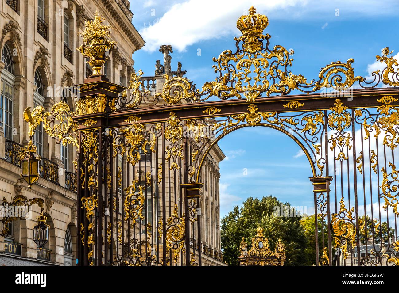 Ein vergoldetes schmiedeeisernes Tor mit einer gekrönten Turmspitze markiert den Eingang zur Place Stanislas in Nancy, Grand Est, Frankreich. Der Schmied Jean Lamour fertigte die Rokoko-Geländer und Tore zwischen 1751 und 1755 für König Stanislas Leszczynski; der Platz ist seit 1983 ein UNESCO-Weltkulturerbe. Stockfoto
