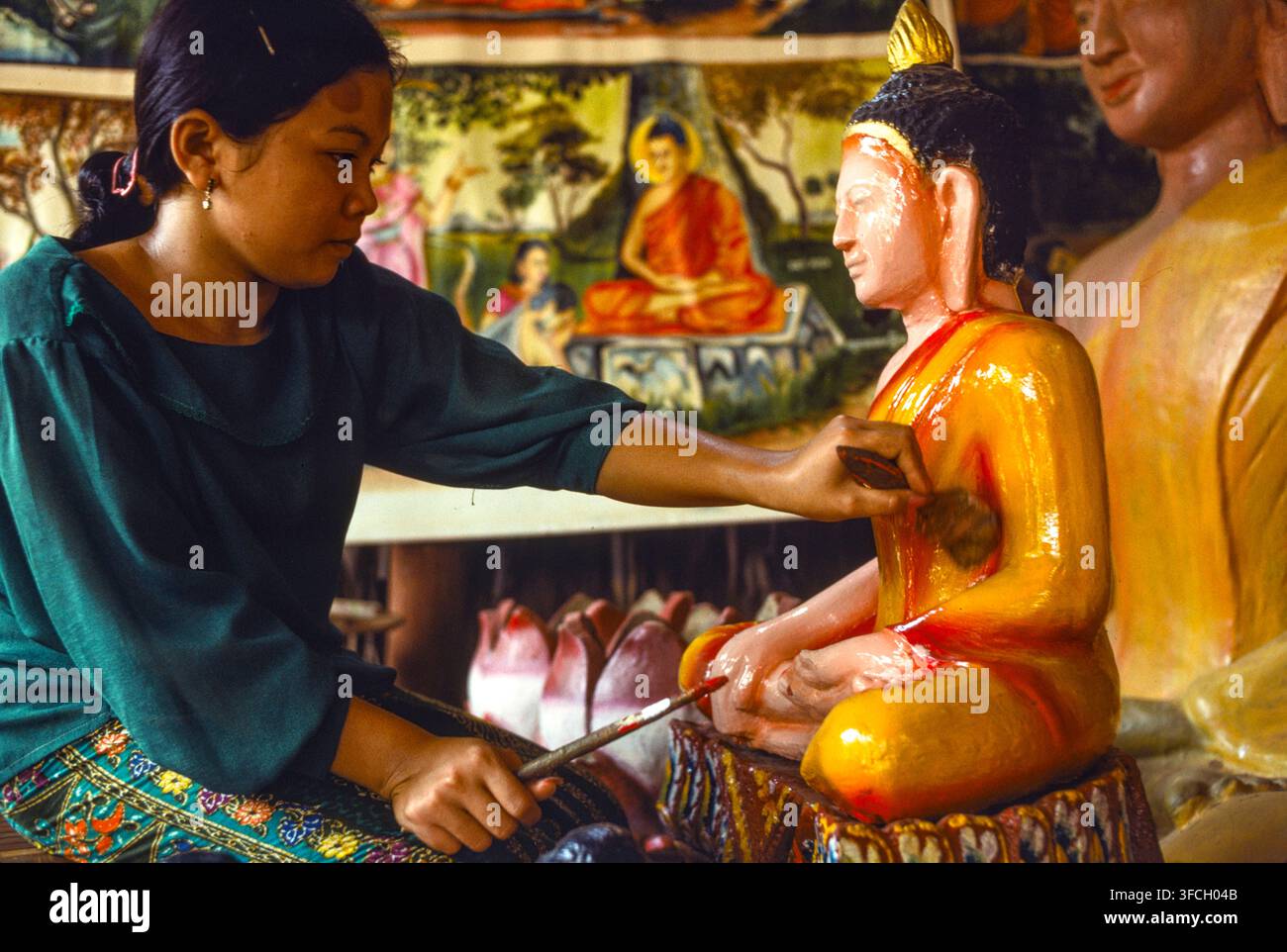 Eine Handwerkerin in einer Werkstatt, die buddhistische Religionsskulpturen herstellt und bemalt, bringt die letzten Retuschen an, Phnom Penh, Kambodscha, Sept. 1988. Stockfoto