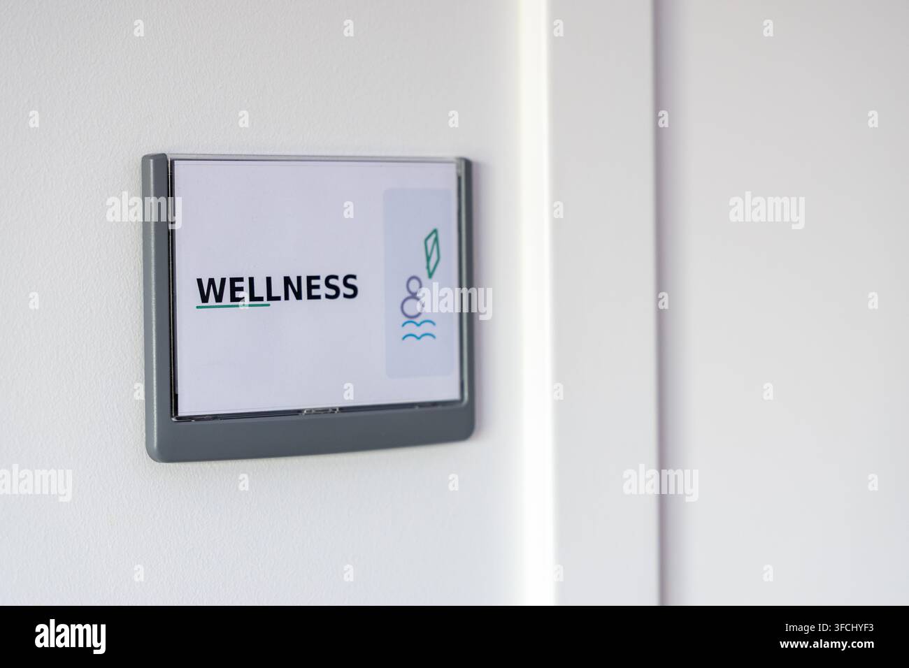Ein modernes Schild mit dem Wort WELLNESS und minimalistischen Symbolen für Wasser und Blatt, montiert auf einer neutralen Wandfläche Stockfoto