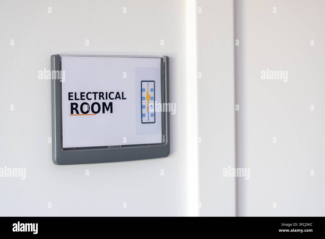 Ein klares Schild an einer weißen Wand kennzeichnet den Stromraum und zeigt Text und eine grafische Darstellung von elektrischen Komponenten Stockfoto