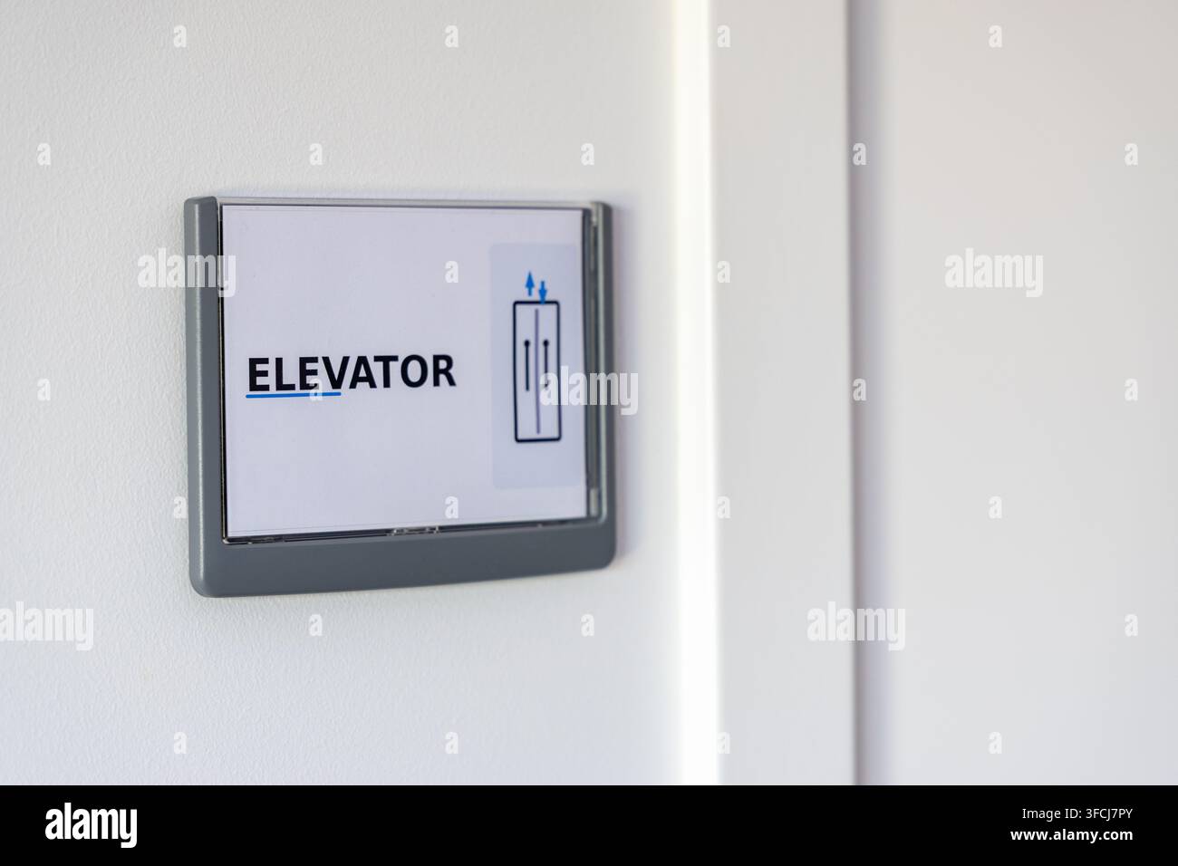 Ein klares Schild, das den Aufzugstandort mit Auf- und Abwärts-Pfeilen anzeigt, montiert auf einer minimalistischen weißen Oberfläche Stockfoto