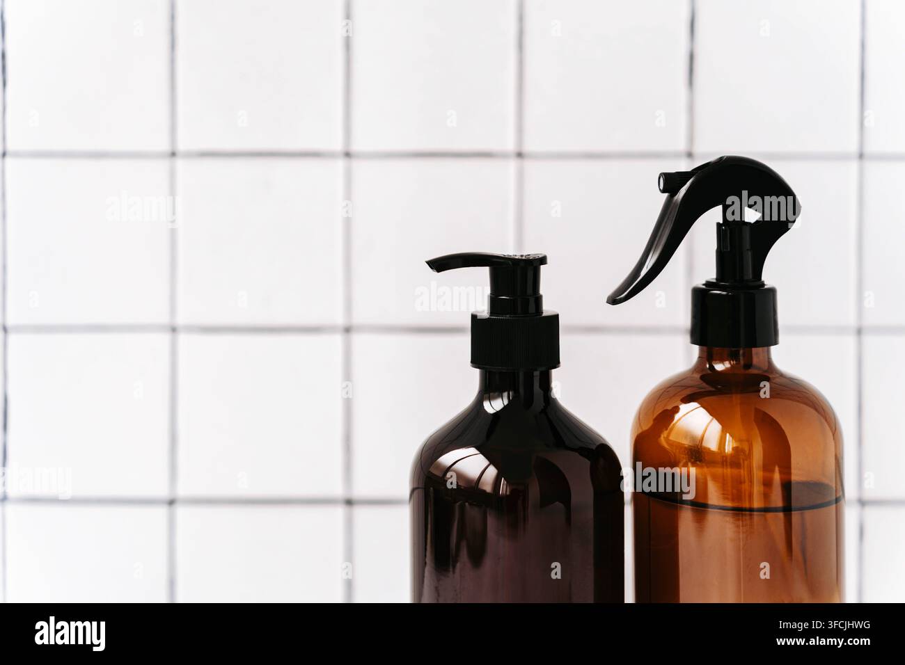 Zwei bernsteinfarbene Glassprühflaschen mit schwarzen Sprühauslösern auf einem sauberen weißen Fliesenhintergrund. Minimale Komposition mit Kopierraum für Reinigung, Kosmetik Stockfoto