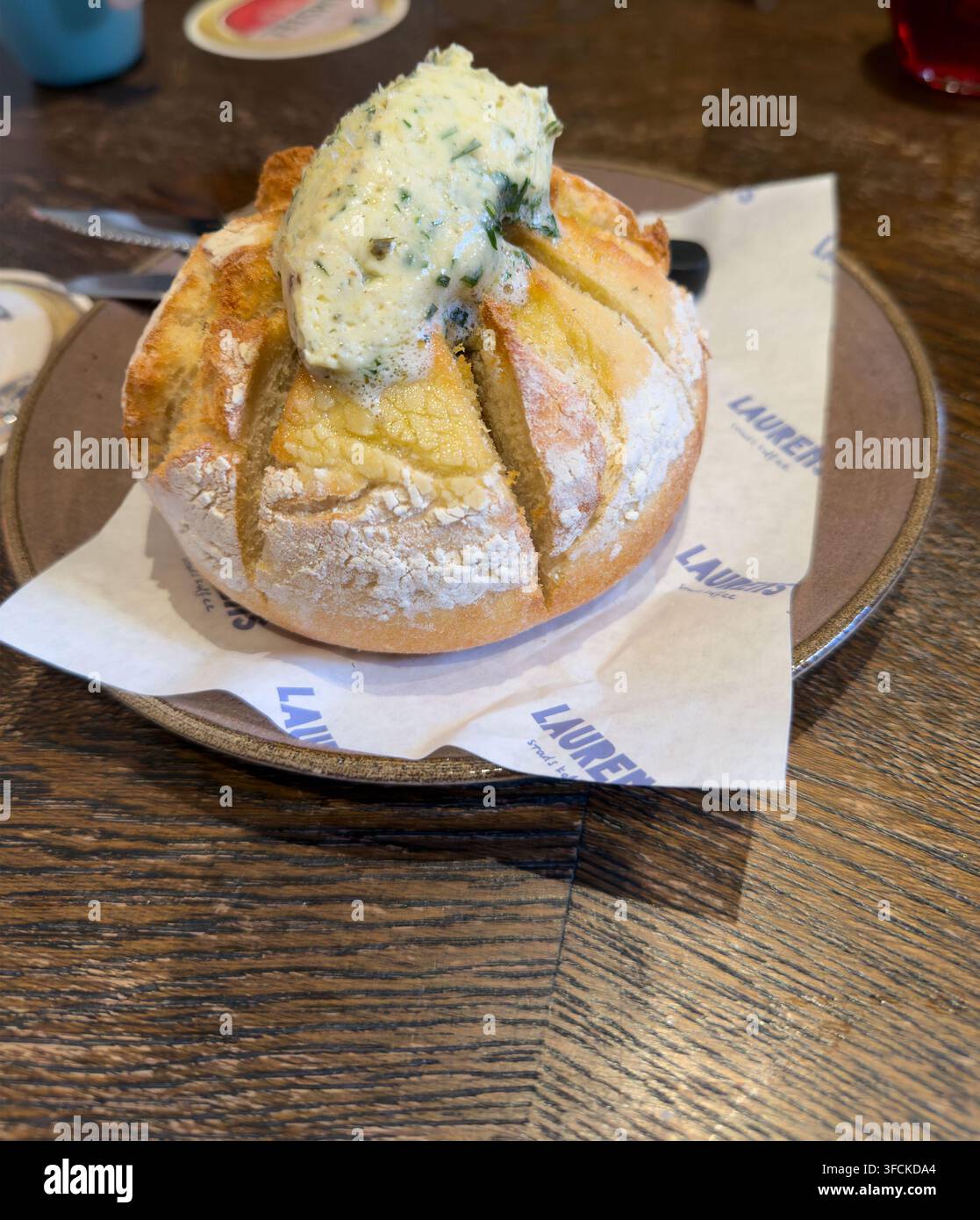 Rundes knuspriges Brötchen mit Knoblauch-Kräuter-Butter auf Laurent-Papier im Café Stockfoto