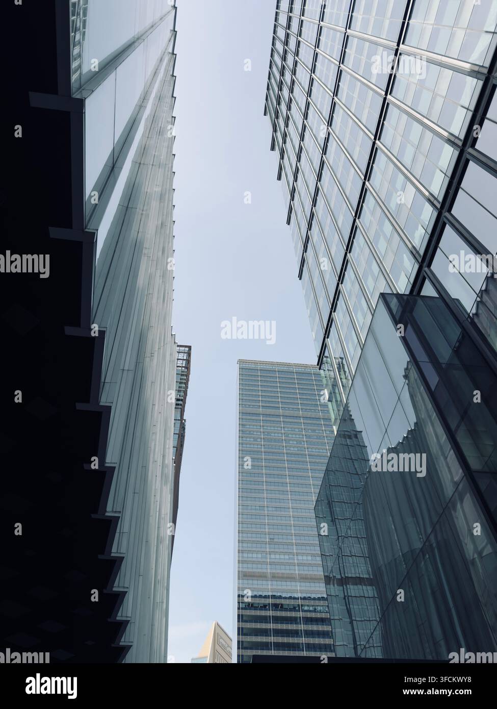 Gläserne Bürotürme erheben sich über einem schmalen Stadtraum und erzeugen starke Reflexionen, geometrische Linien und eine aufwärtsgerichtete architektonische Perspektive. - Smartphone-aufgenommenes Stockfoto