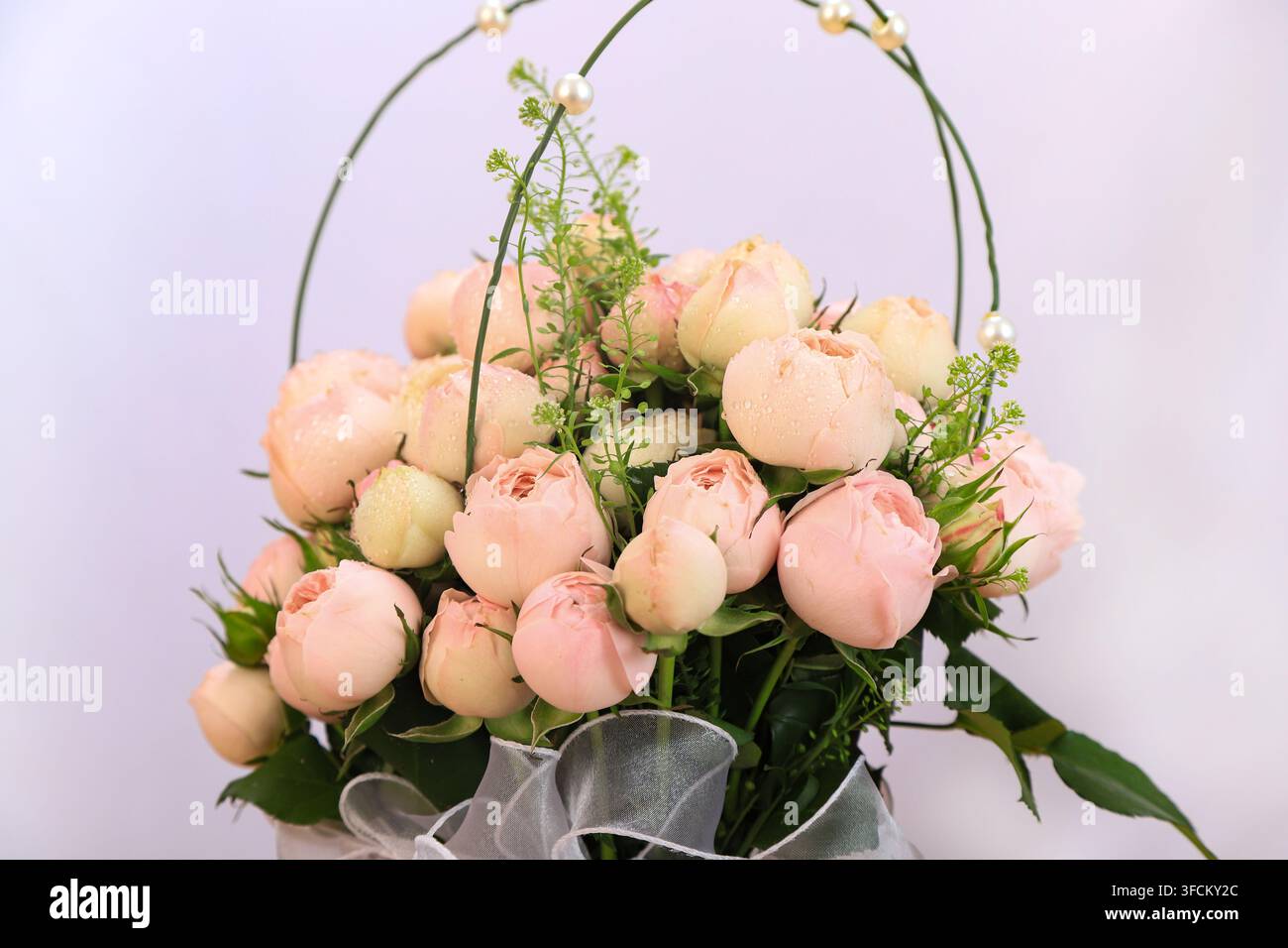 Nahaufnahme eines wunderschönen Straußes aus champagnerfarbenen Rosen mit Tautropfen auf den Blütenblättern. Verziert mit Perlen und zarten Ranken, ist das Arrangement eingefangen Stockfoto