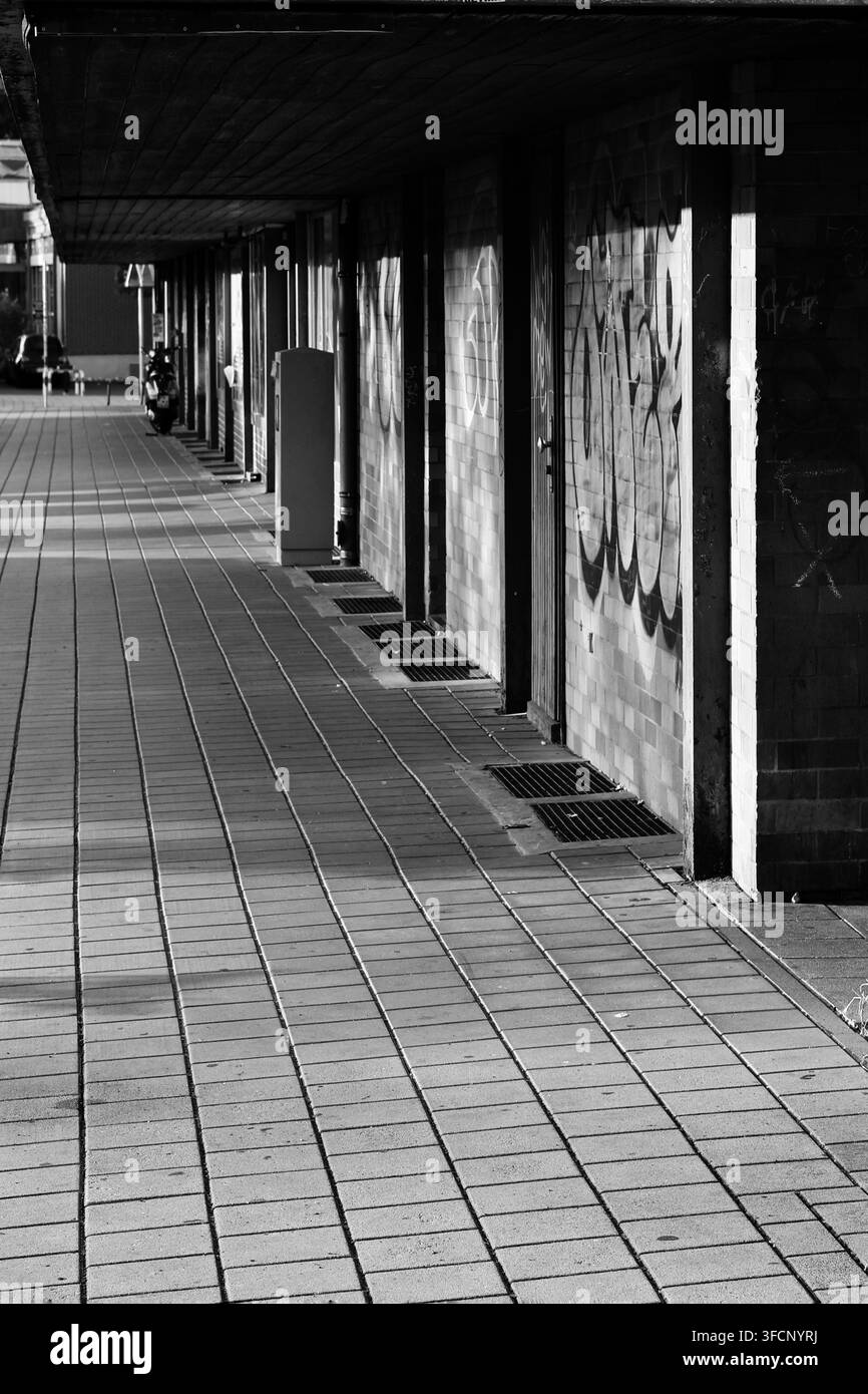 Städtischer überdachter Gehweg mit graffiti-bezogenen Ziegelwänden und starker geometrischer Perspektive in Schwarzweiß Stockfoto