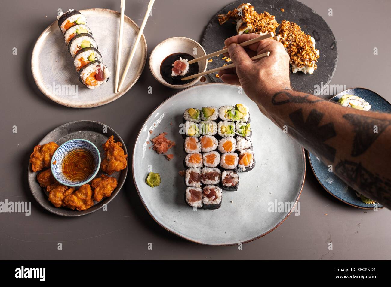 Hand, die Sushi-Rollen mit Stäbchen an einem japanischen Esstisch auswählt Stockfoto