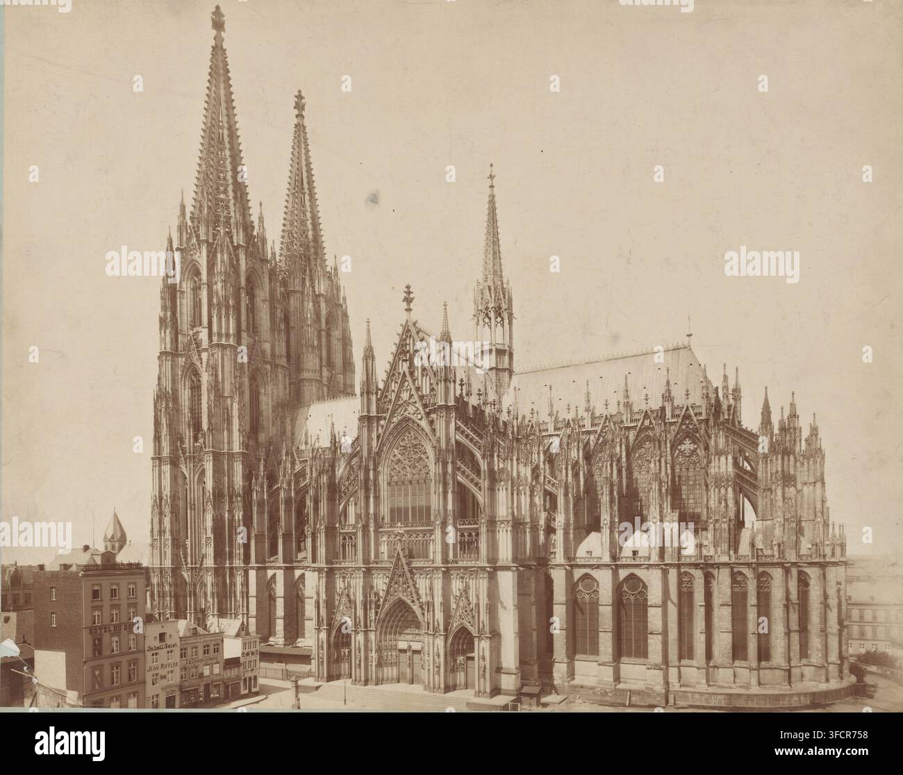 Ansicht des Kölner Doms, Fotografie, Köln, 1880 - 1910, Fotograf, Nordrhein-Westfalen, Papier, Karton, Albumen-Druck, Höhe 445 mm x Breite 610 mm, Kirche (Außenansicht), Kölner Dom. Eine große gotische Kathedrale füllt das Bild mit hohen spitzen Türmen, kunstvollen Steinverzierungen und gewölbten Fenstern; aufwendige Bildhauereien und dekorative Fialen schmücken die Fassade und die Dachlinie, einschließlich eines markanten zentralen Eingangs mit aufwendiger Steinarbeit und durch die Bögen sichtbaren Buntglasfenstern; Strebepfeiler und Strebebögen erheben sich an den Seiten und stützen Reihen hoher Lanzettfenster; Stockfoto