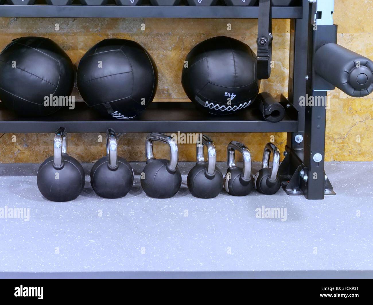 Saubere organisierte Darstellung von Fitnessgeräten mit schweren schwarzen Medizinbällen auf einem Metallregal und einer ordentlichen Reihe von Kettlebells mit Chromgriffen auf dem Boden Stockfoto