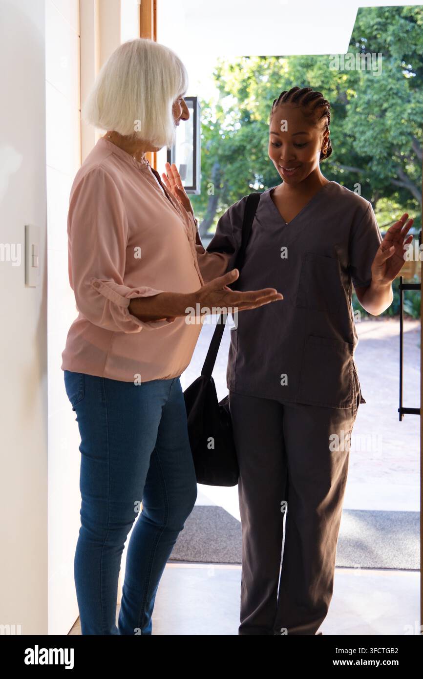 Senior White-Frau und erwachsene afroamerikanische Betreuerin sprechen an der offenen Tür, Fußabtreter, schwarze Tasche Stockfoto