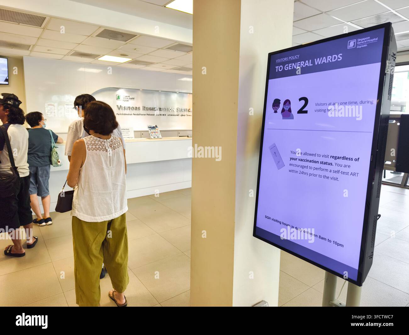 Lobby des Singapore General Hospital mit Besuchern, die in der Nähe eines Tresens und eines digitalen Schildes stehen, das Besucherinformationen für die allgemeinen Stationen anzeigt Stockfoto