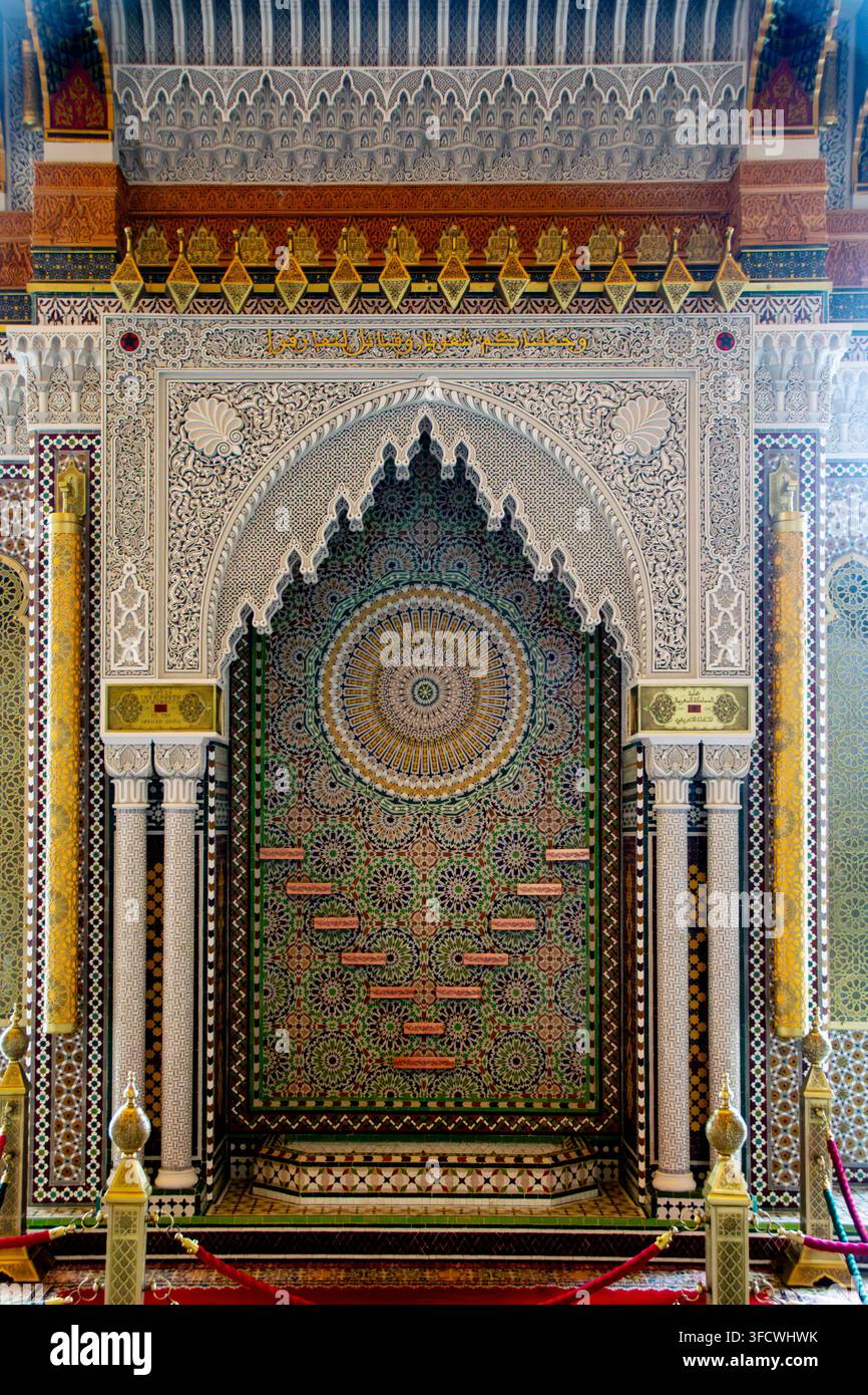 Große islamische Gebetsnische, kunstvoll gekachelter Torbogen mit geometrischen Mustern. Goldene Akzente umrahmen das zentrale Mihrab, vor dunklem Grün und Wei Stockfoto