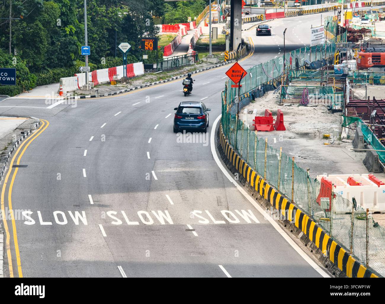 Nicoll Highway, Singapur, Baustelle mit Sicherheitsbarrieren und einem vorausfahrenden Auto, Straßeninfrastrukturentwicklung, „SLOW“-Bodenmarkierungen Stockfoto