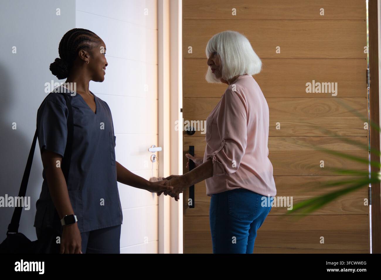 Afroamerikanische Krankenschwester in dunkler Kleidung, die im Foyer an der Eingangstür die Hand einer älteren Frau hält Stockfoto