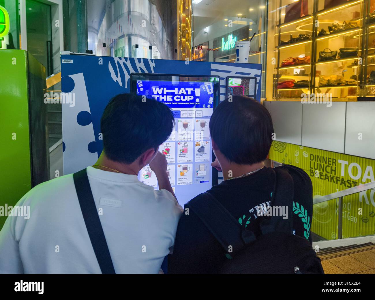 zwei Personen, die einen großen blauen What The Cup!-Smart-Vending-Automaten mit über 300 anpassbaren Getränkeauswahlmöglichkeiten nutzen, Singapur Stockfoto