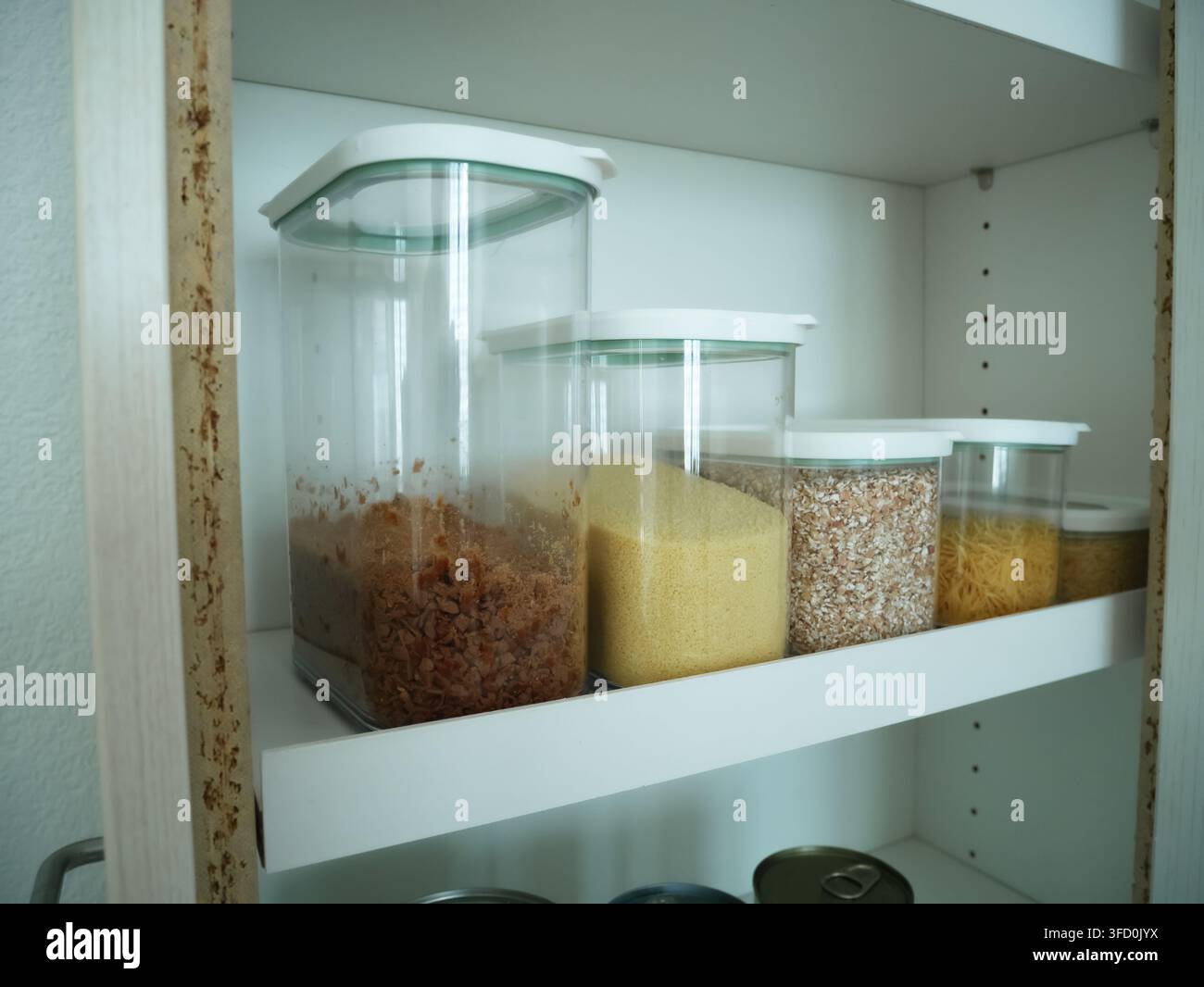 Mehrere klare Glasvorratsbehälter, gefüllt mit verschiedenen Trockenwaren und Müsli, ordentlich auf einem Küchenregal organisiert. Zeigt eine effektive Vorratskammerorganisation Stockfoto